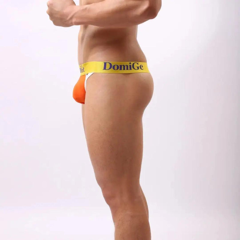 Model wearing DomiGe T-back thong — logo waistband side angle orange