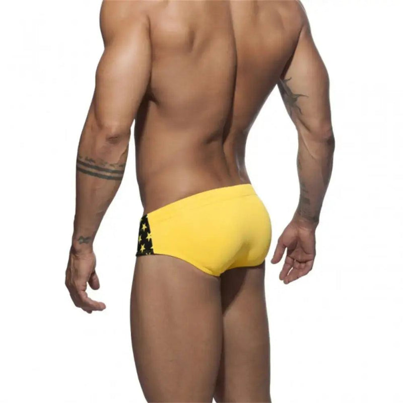 DomiGe flag print swim briefs in yellow — model rear view	
