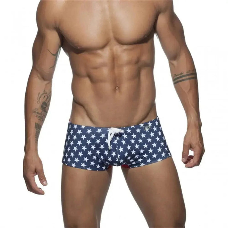 DomiGe men's flag print swim trunks in blue — model front view showing low-rise square leg cut and colorblock design	