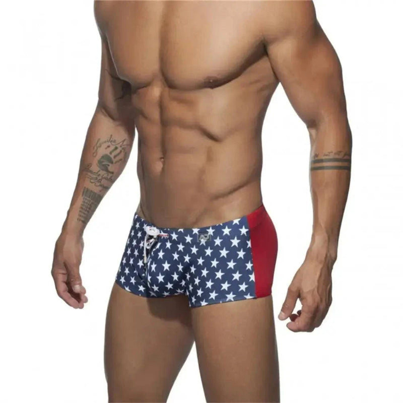 DomiGe men's flag print swim trunks in blue — model side view showing drawstring waistband and fit	