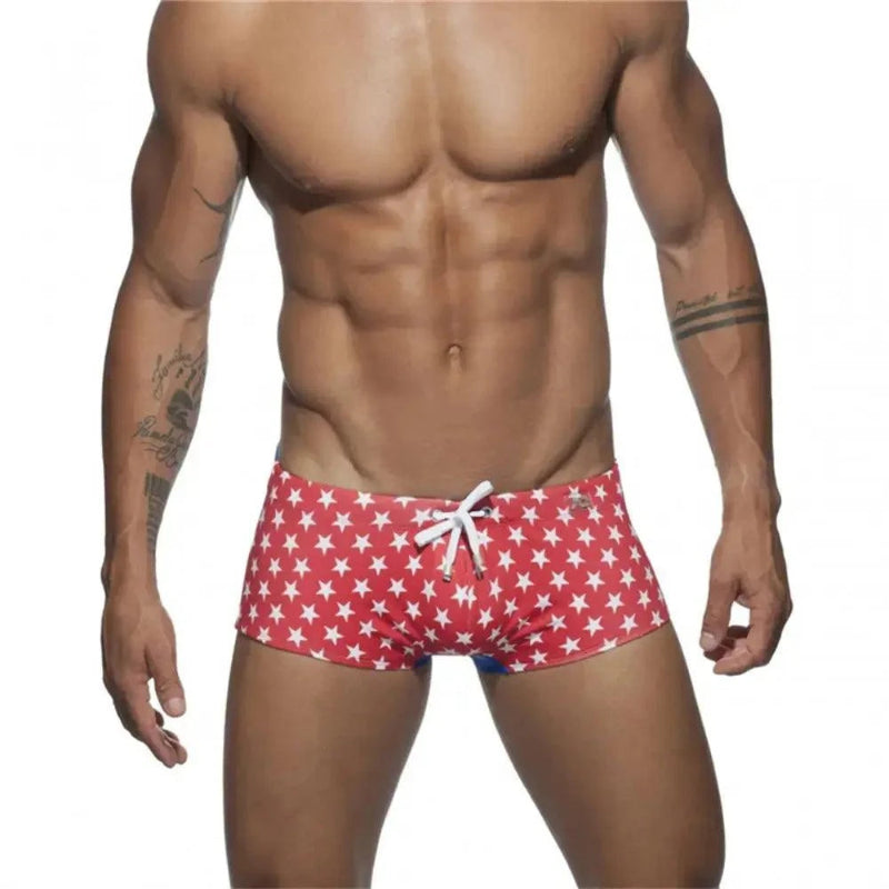 DomiGe men's flag print swim trunks in red — model front view showing bold national flag colorblock pattern	