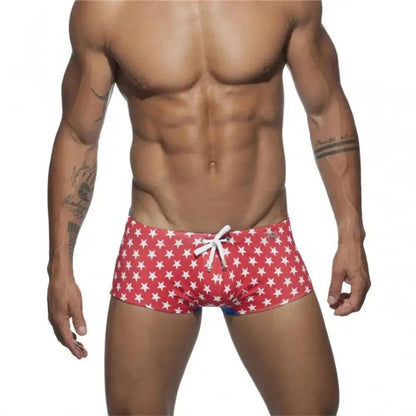 DomiGe men's flag print swim trunks in red — model front view showing bold national flag colorblock pattern	