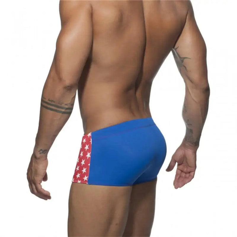 DomiGe men's flag print swim trunks in red — model rear view showing square leg silhouette	