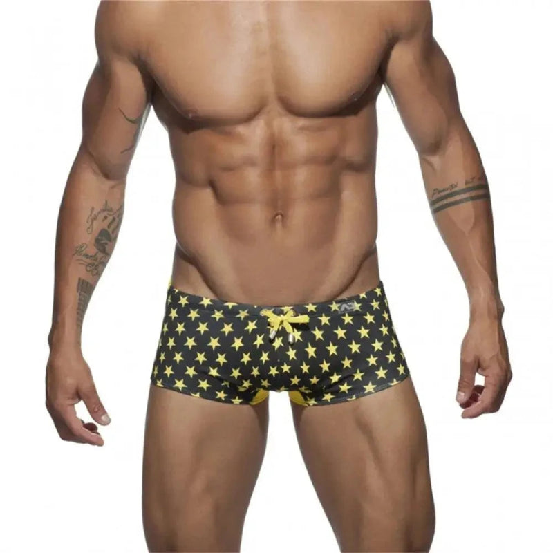 DomiGe men's flag print swim trunks in yellow — model front view showing vibrant colorblock print	