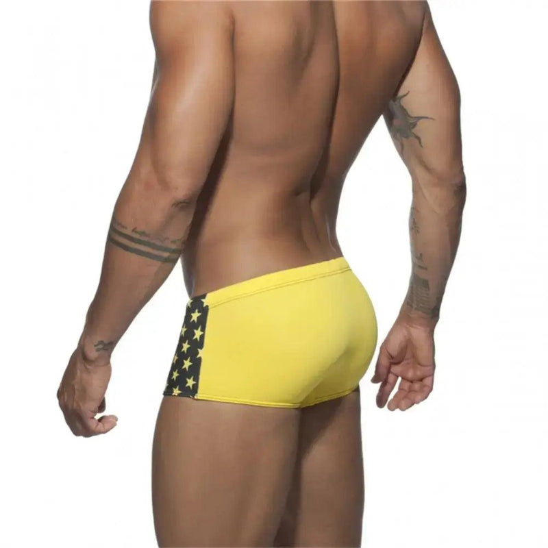 DomiGe men's flag print swim trunks in yellow — model rear view showing square leg cut and fabric	