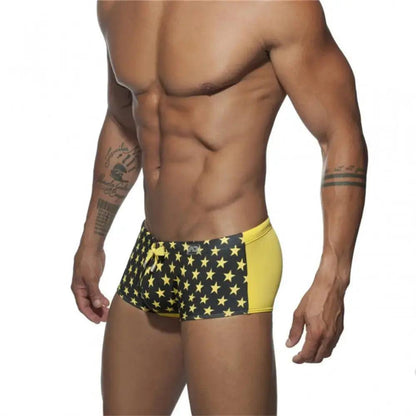 DomiGe men's flag print swim trunks in yellow — model side view showing drawstring and elastic waistband	